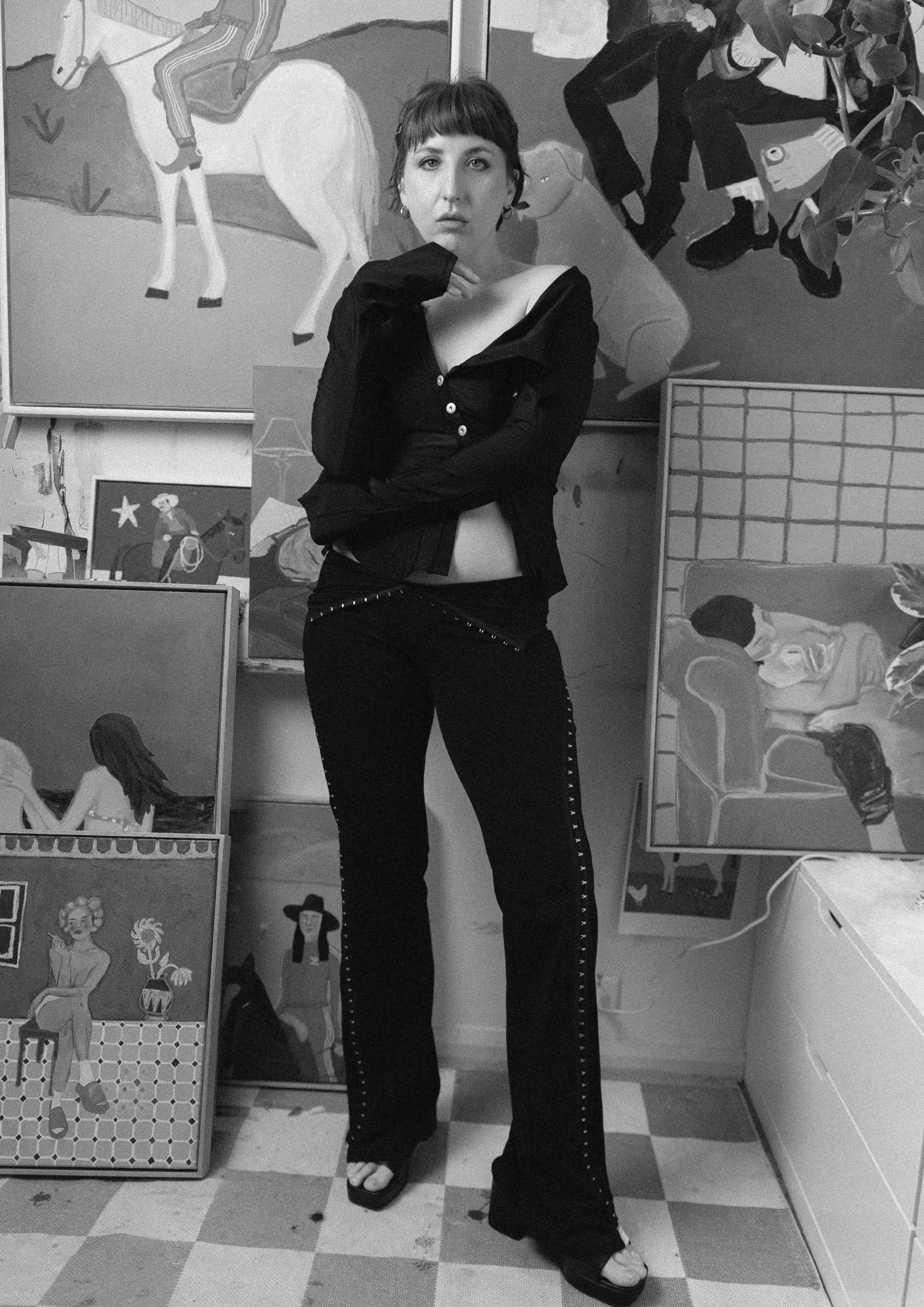 Artist Kasia Frankowicz in a stylish outfit  by Karlaidlaw standing in a room with various artworks on the wall.
